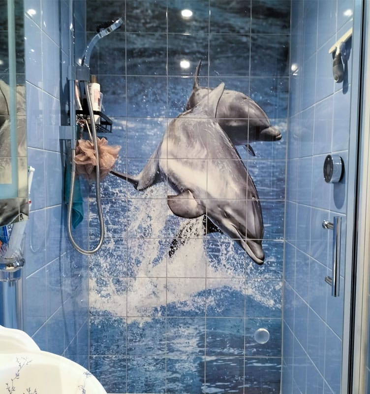 Printed Tiles 9 A shower with bespoke blue tiles features a mural of two dolphins jumping out of water. The shelves inside hold toiletries and a loofah. A shower with bespoke blue tiles features a mural of two dolphins jumping out of water. The shelves inside hold toiletries and a loofah.